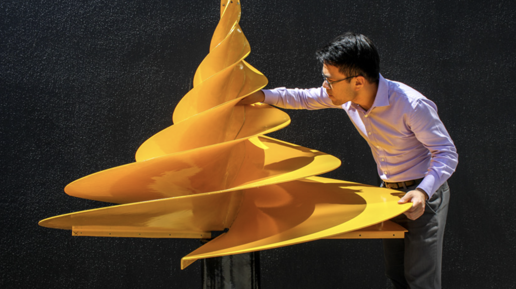 A man examining a yellow Composite Hydro-Electric Turbine against a black background