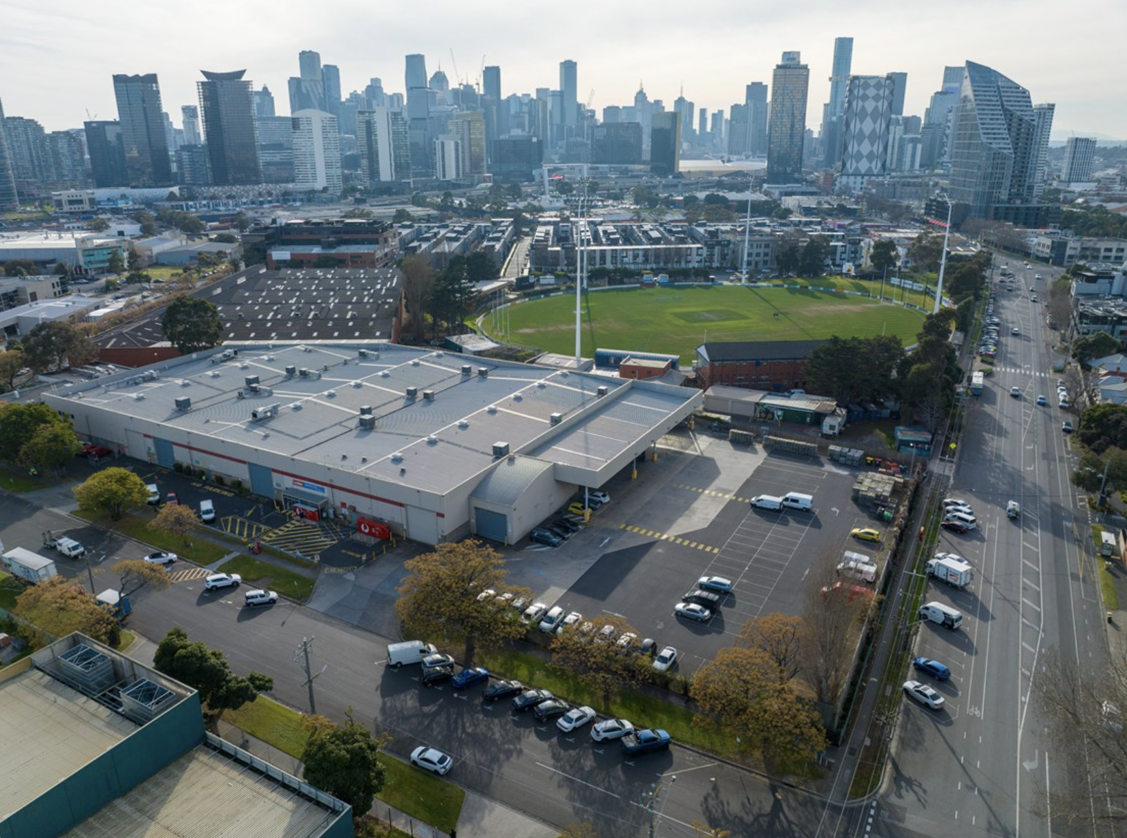 Aerial view of Fishermans Bend featuring industrial buildings, a sports ground, suburbs, all the way to the Melbourne skyline during the day