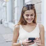 A woman on a street smiling at her mobile phone