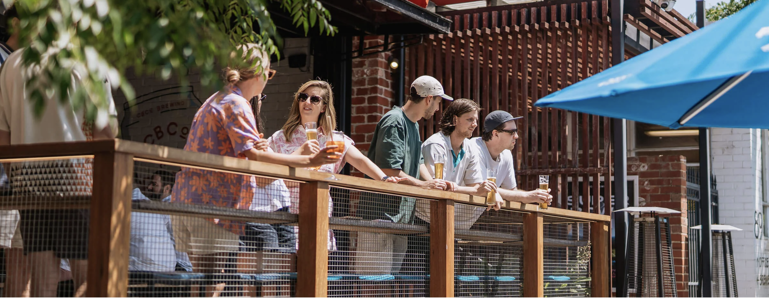 A group of people stand at a balcony drinking in the sun